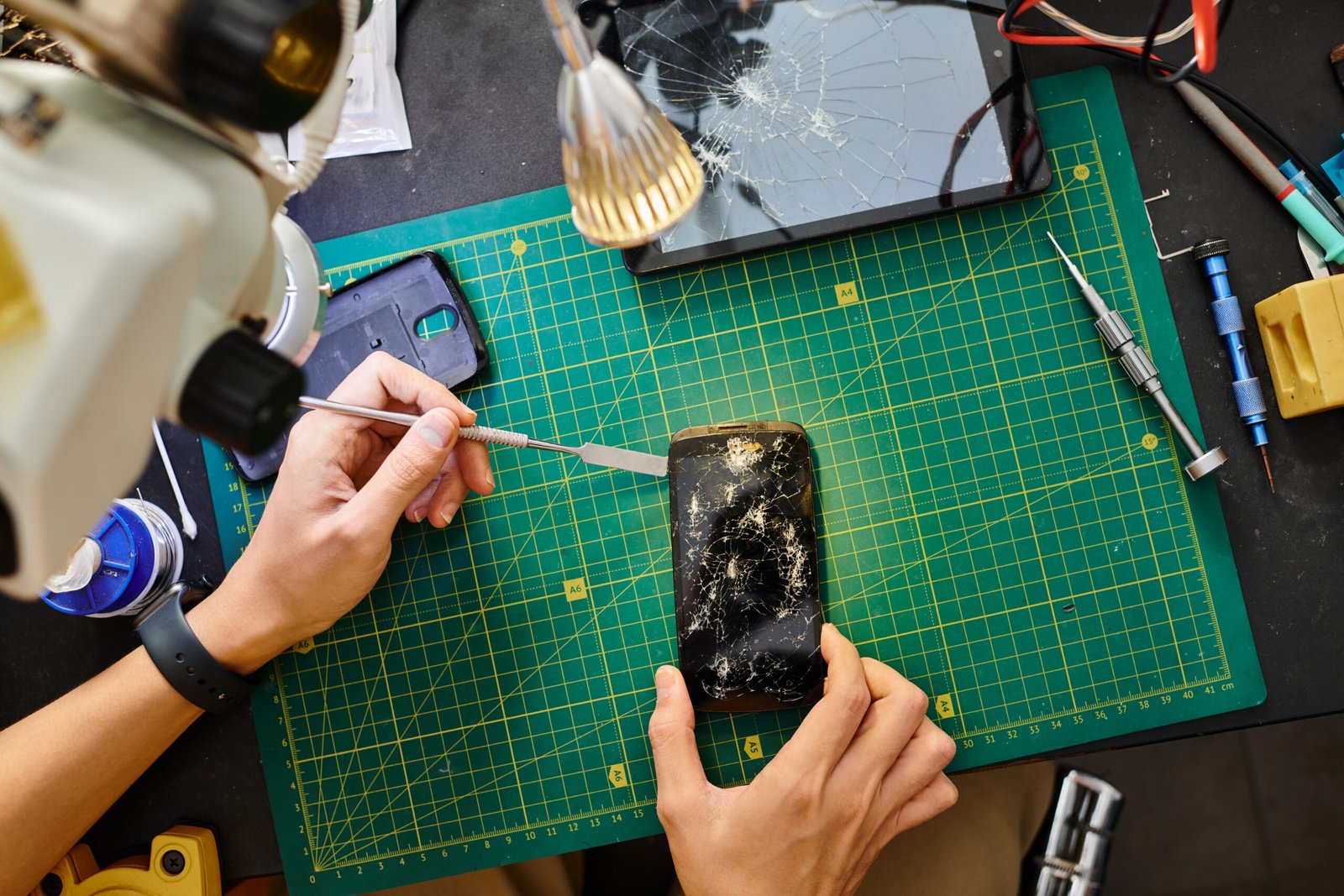 cropped view of repairman removing broken touchscreen of smartphone in maintenance workshop